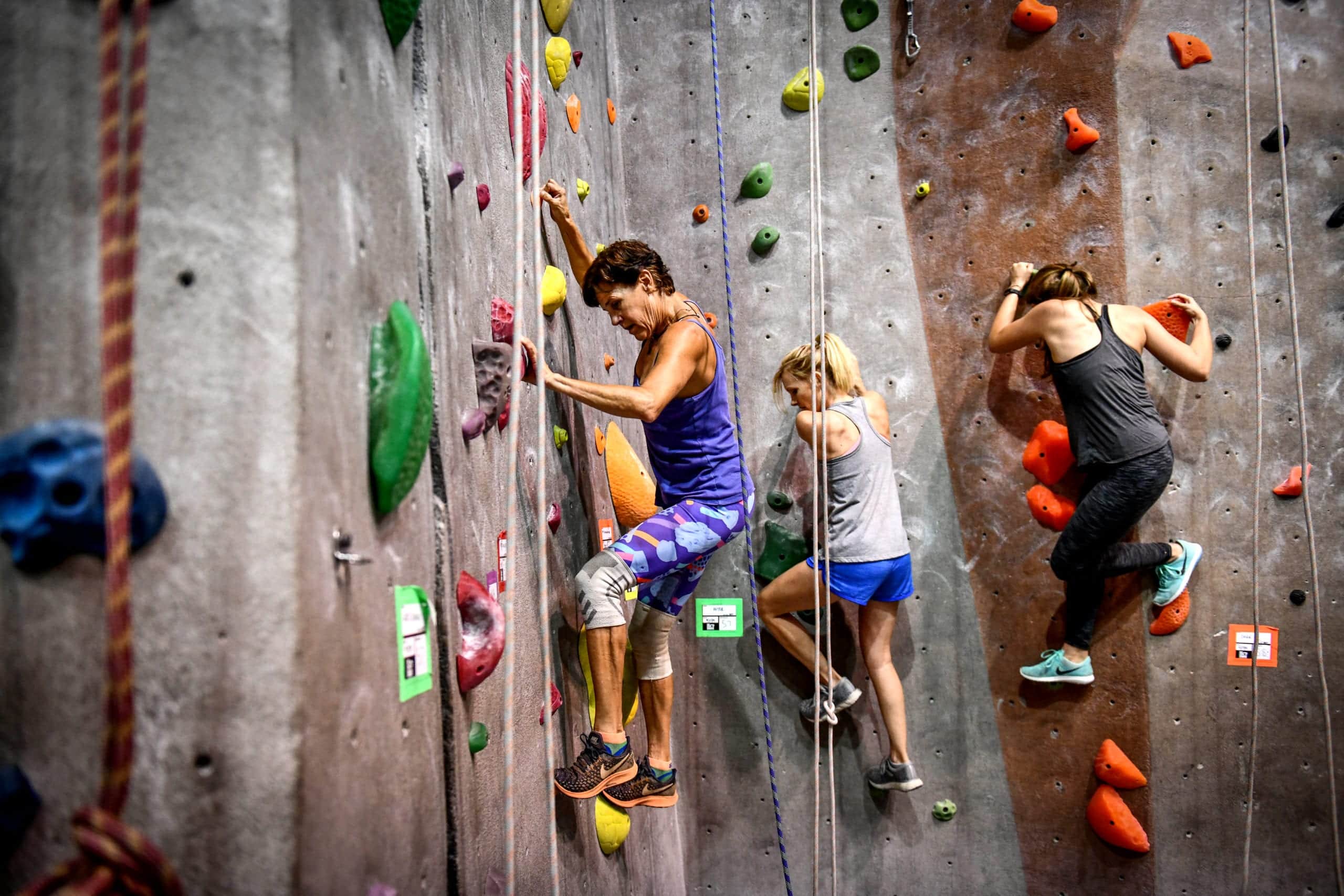 Beautiful young woman in black outfit climbing on practical wall in gym,  bouldering, extreme sport, rock-climbing concept Stock Photo